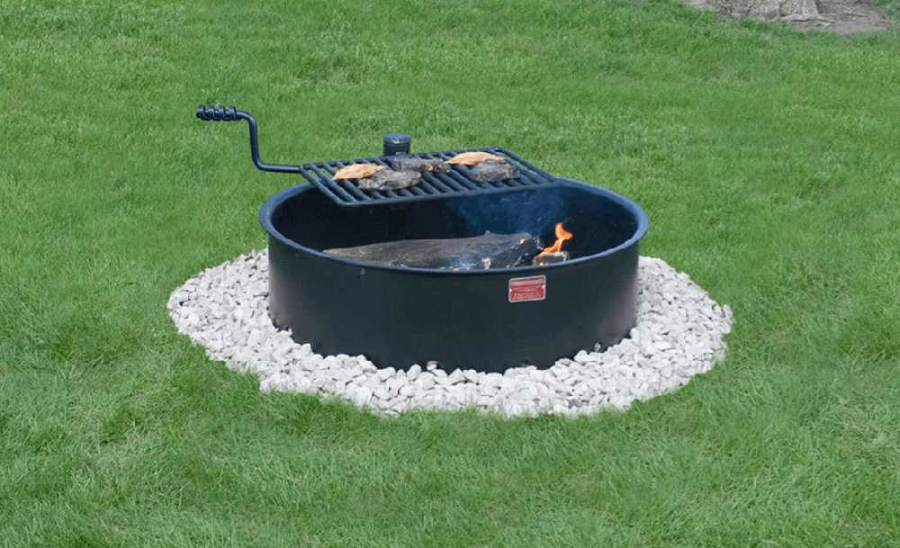 Commercial fire ring park grill with swing-away cooking grate installed in a grassy outdoor setting for campfire cooking and controlled open flame use